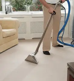 Professional carpet cleaner using a hot-water extraction wand and hose machine in a living room in Lowell, MA.