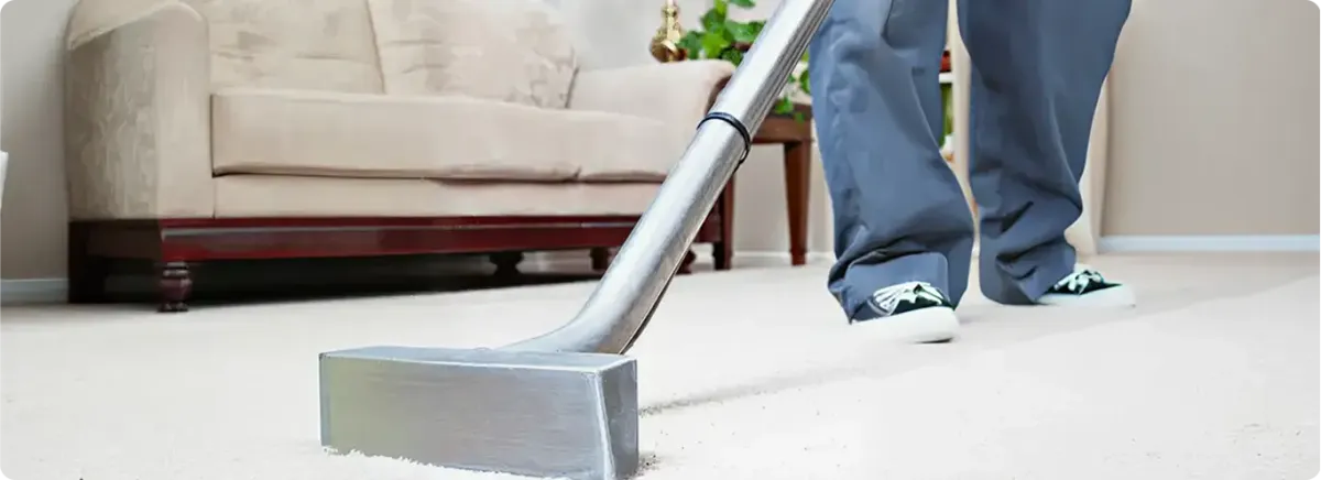 Carpet cleaning technician using a hot-water extraction wand on a light-colored carpet in a living room, Lowell, MA.