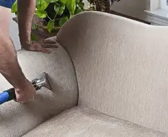 Professional upholstery cleaner deep-cleaning a fabric sofa with a handheld extraction tool and hose in Lowell, MA.